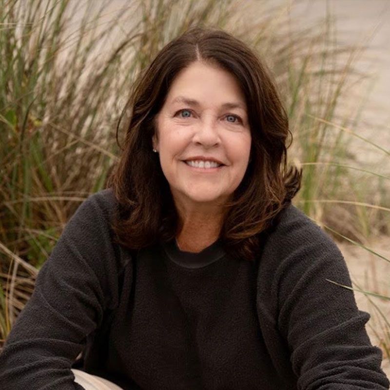 Smiling person in a dark sweater seated outdoors among tall grass