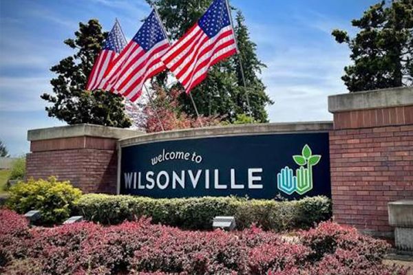 Welcome to Wilsonville sign with American flags and flowers at the entrance