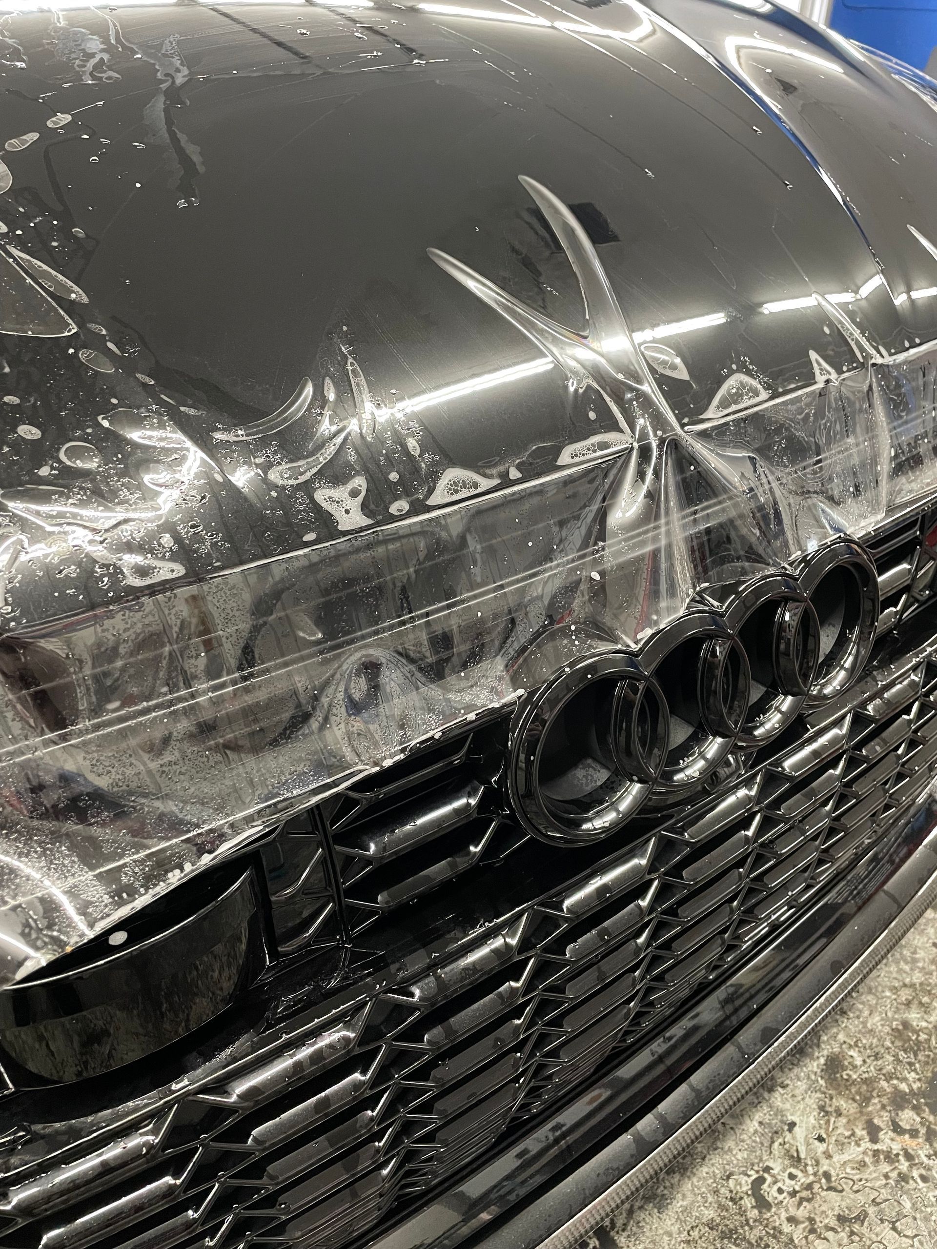 A close up of a black car with a hood covered in plastic.