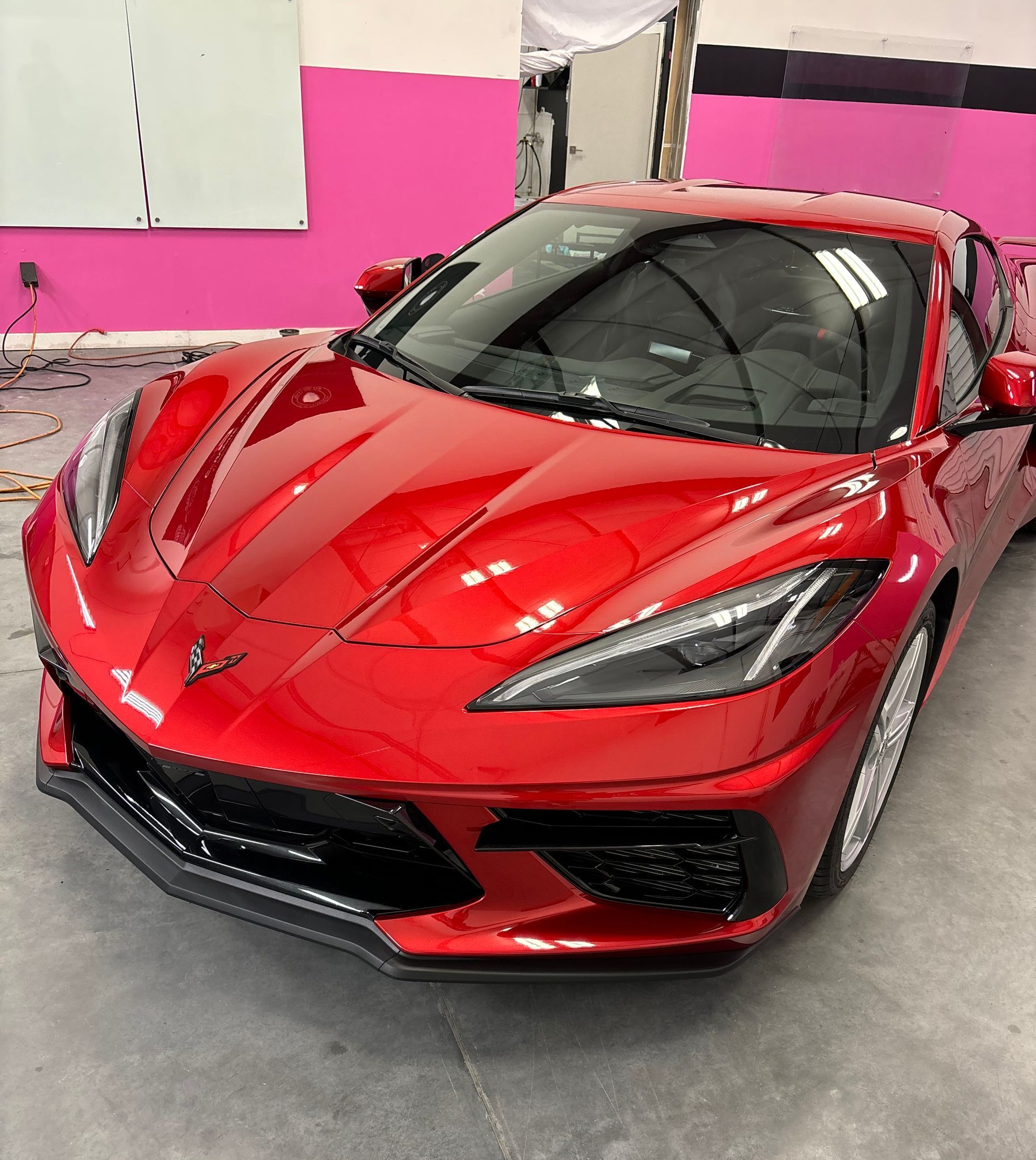 Red Chevrolet Corvette sports car parked in a garage with pink walls.