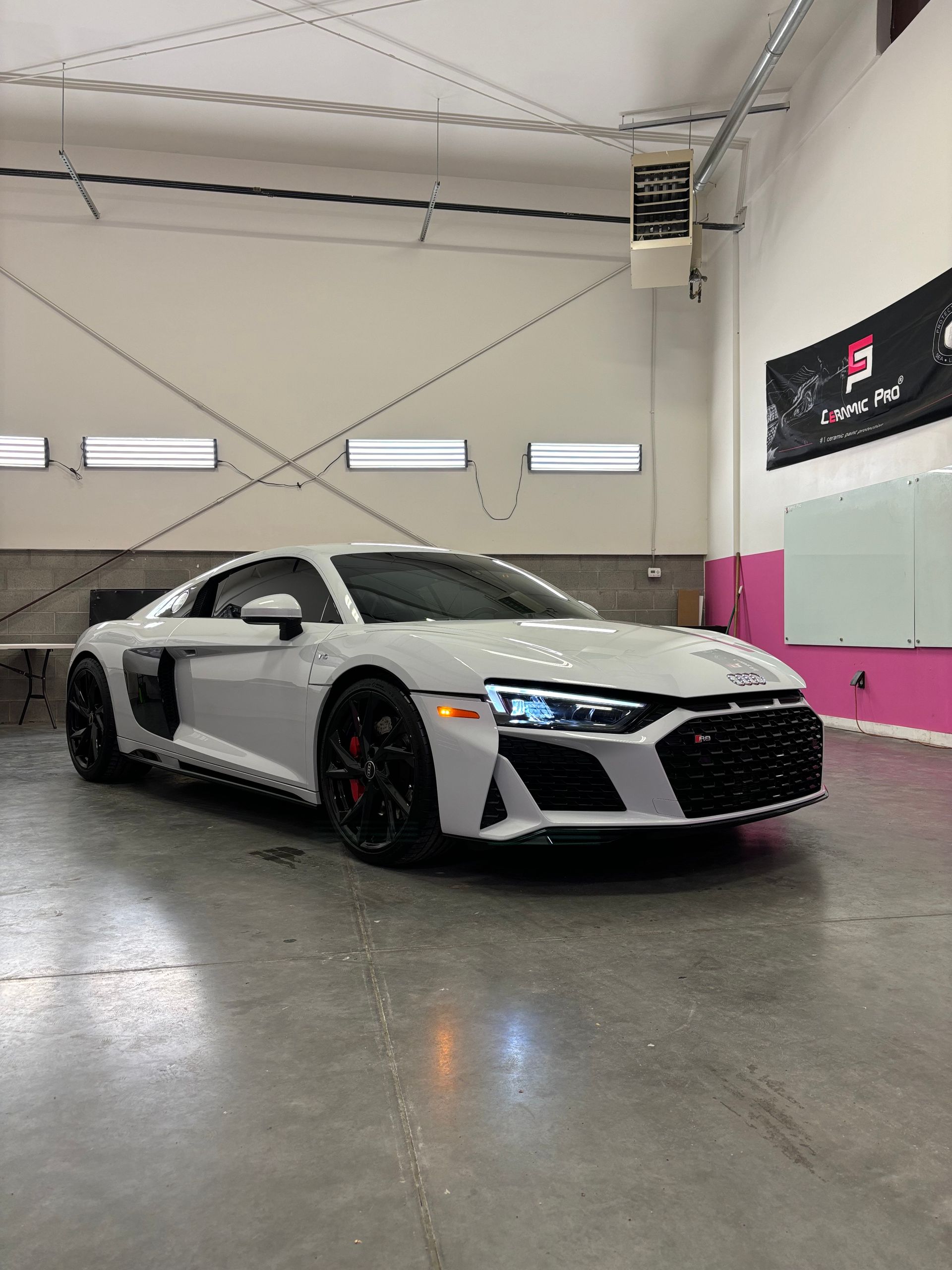 Gray Audi R8 sports car parked inside a garage, black wheels and red brake calipers, white building interior.
