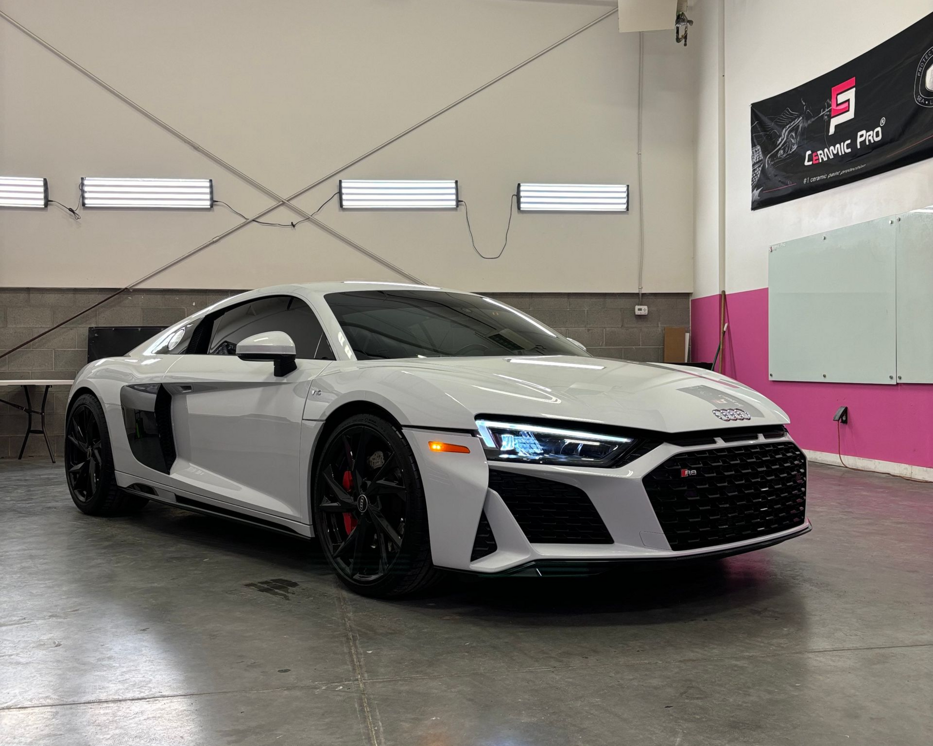 White Audi R8 sports car in a garage with black wheels and red brake calipers.