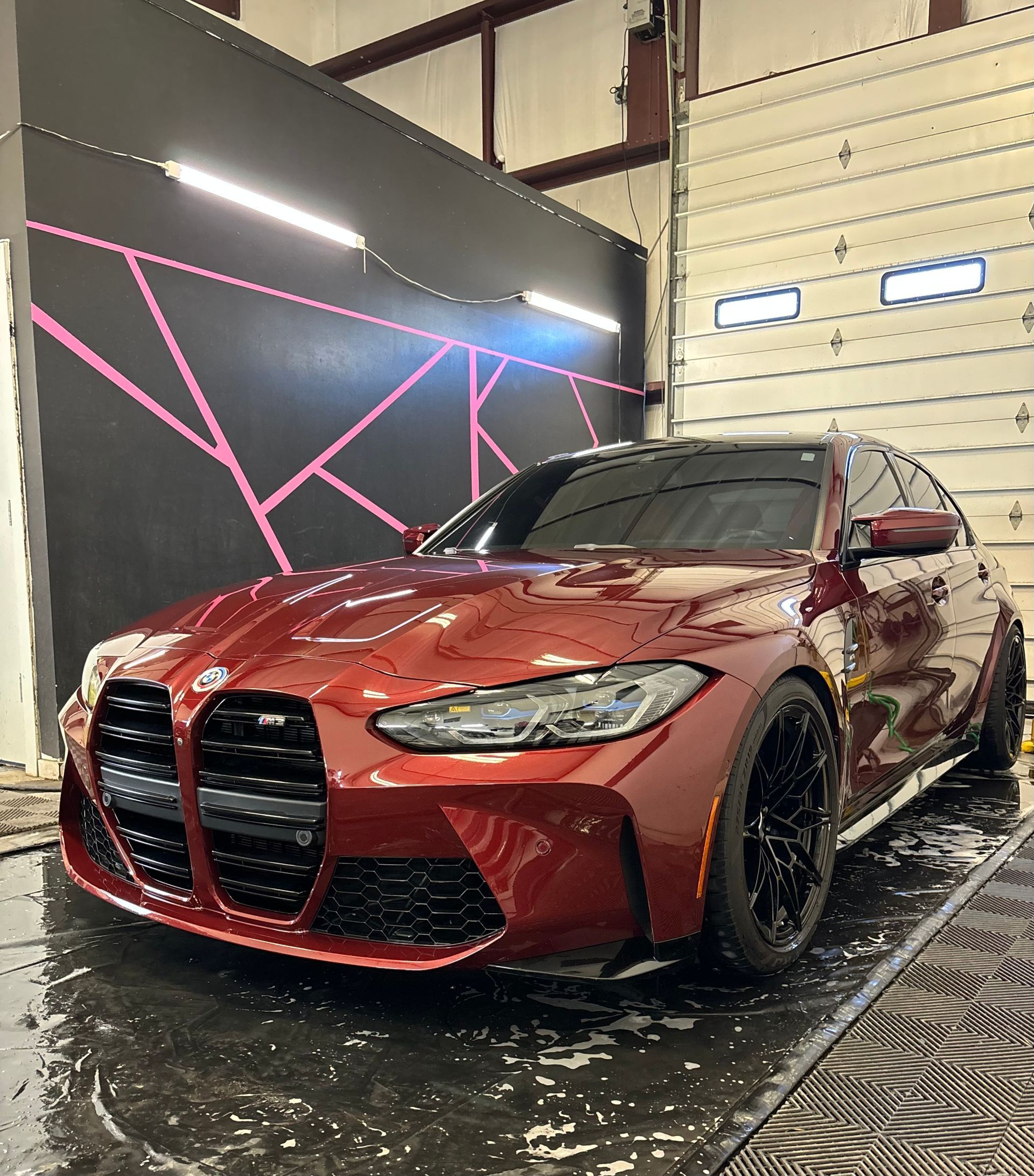 Red BMW sedan being washed inside a garage; water droplets visible.