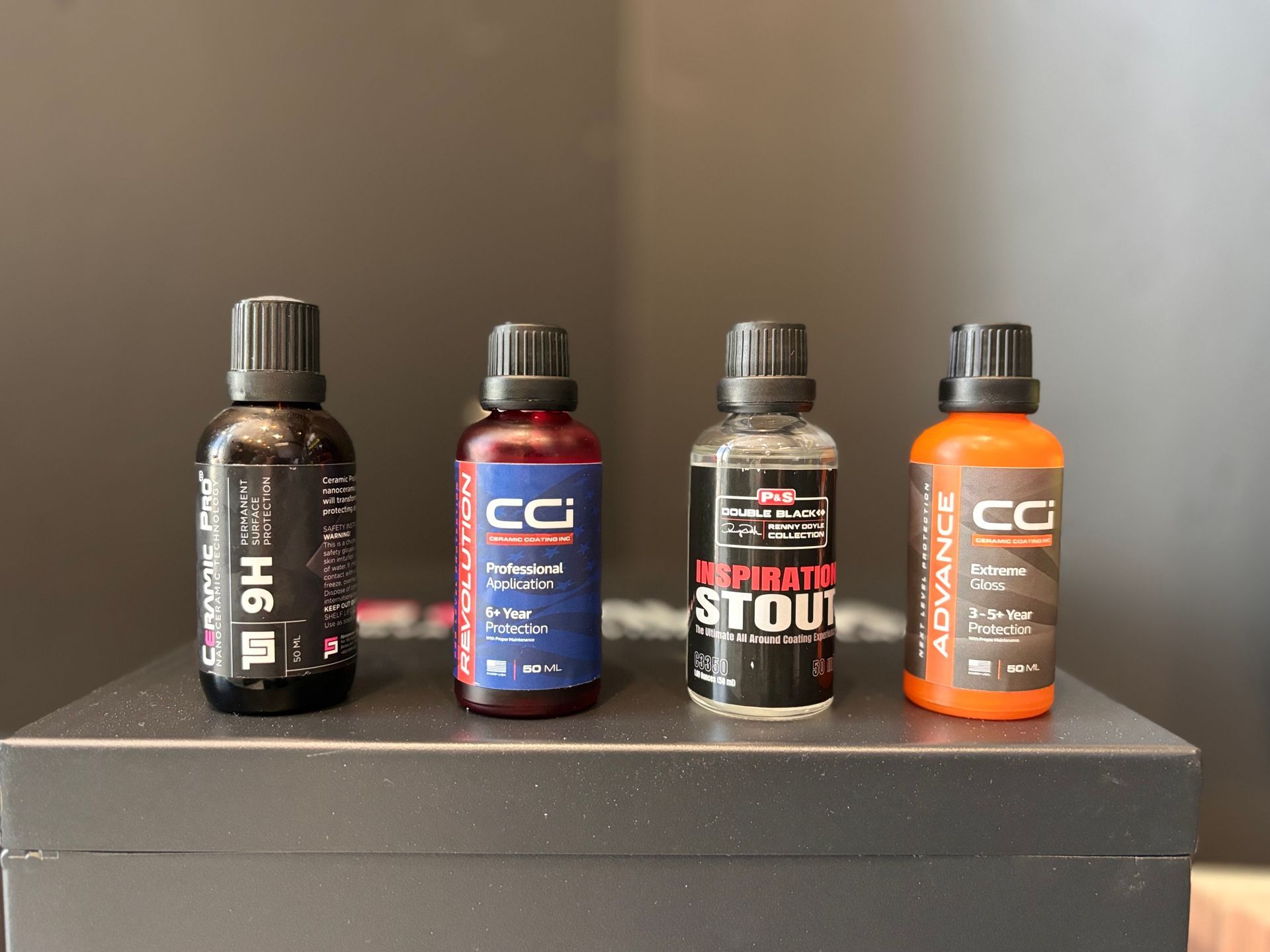 Four bottles of car detailing products lined up on a dark surface.