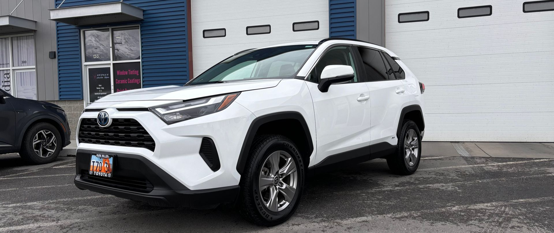 White Toyota RAV4 SUV parked in front of a building with a blue facade and a garage door.