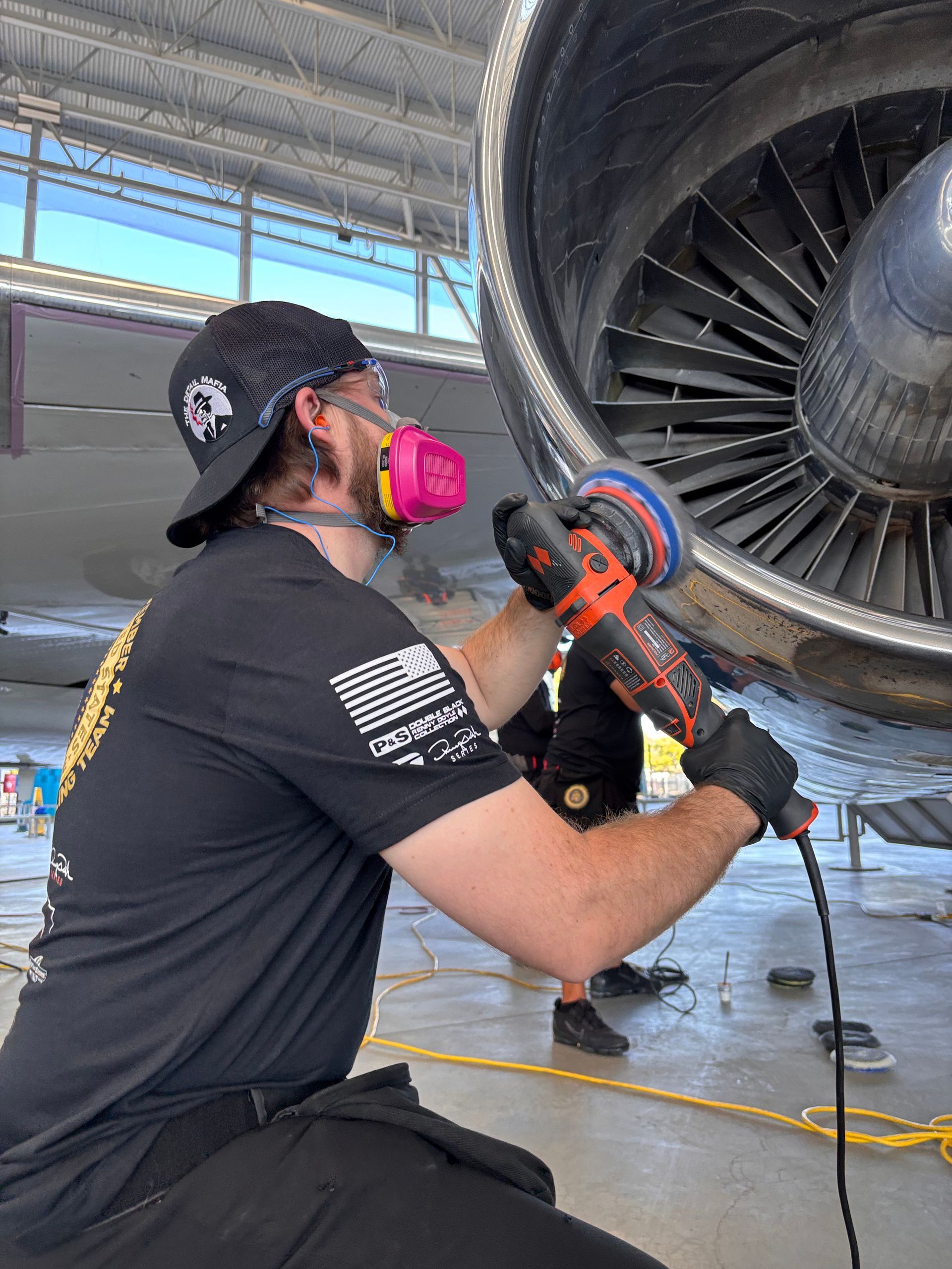Man with respirator sanding an aircraft engine in a hangar.