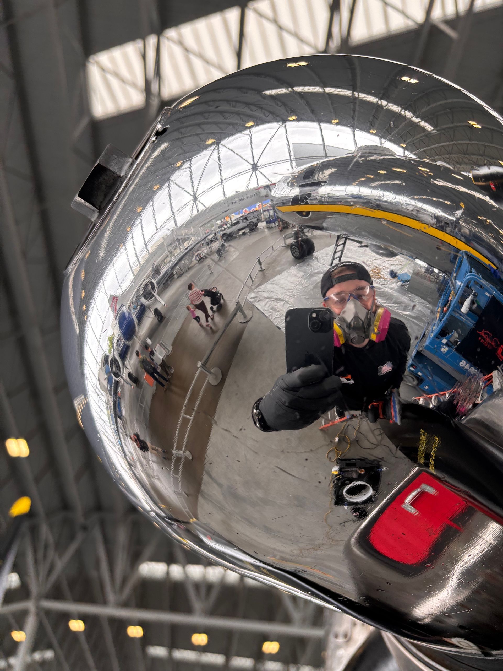 Shiny metal surface reflecting a person in a mask taking a selfie, industrial setting.