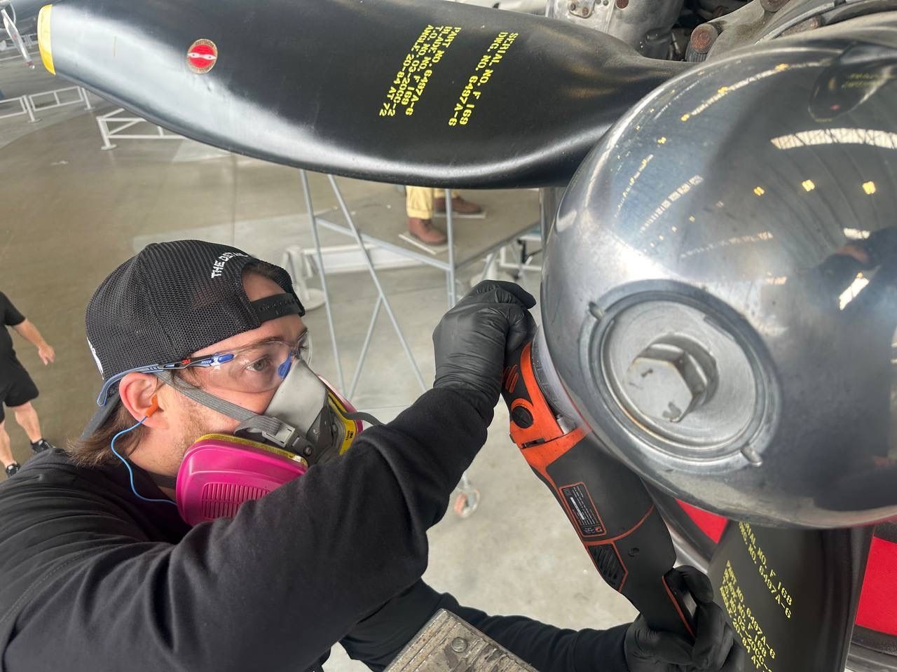 Person working on an aircraft propeller, wearing safety glasses and a respirator.