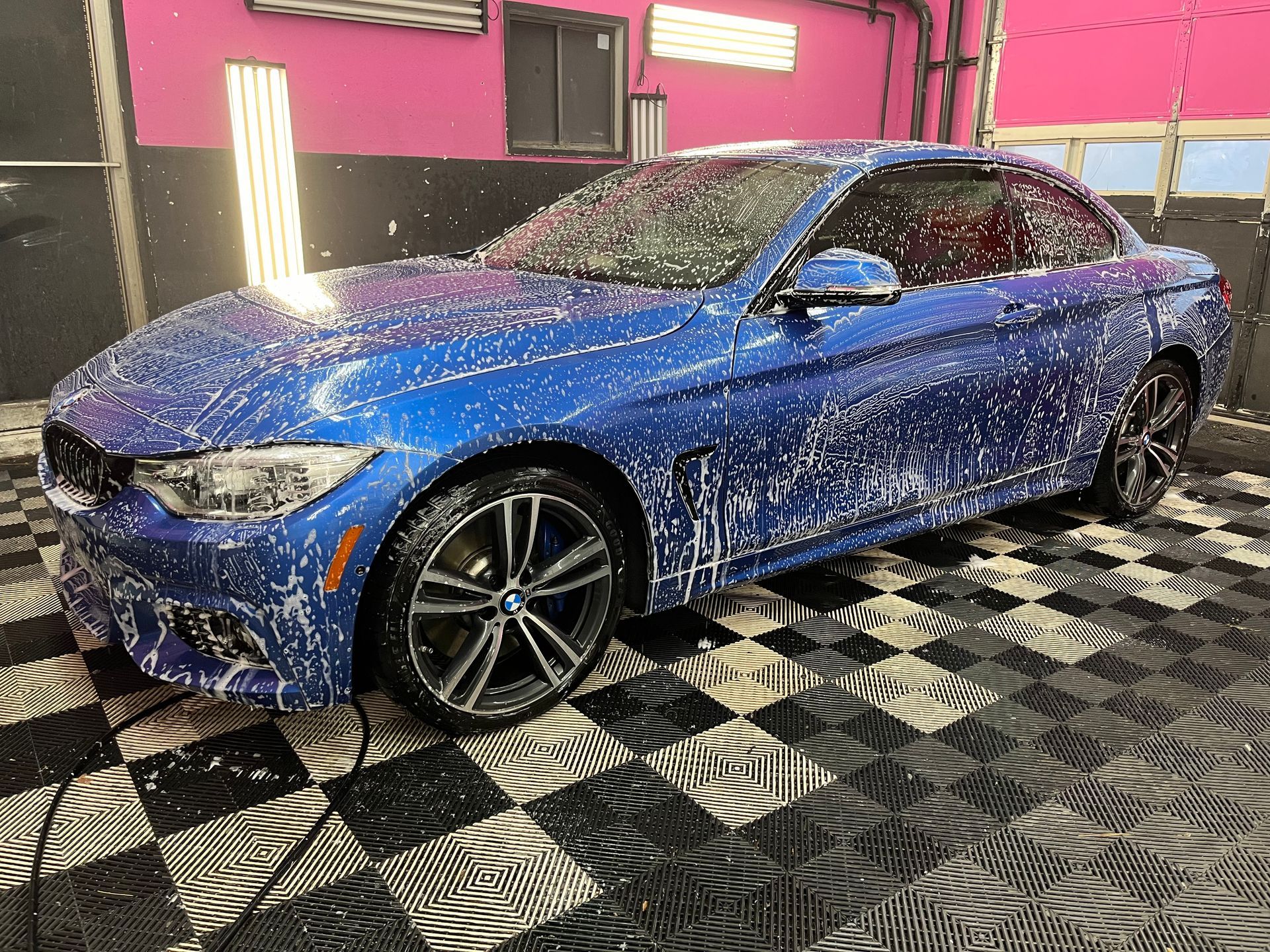Blue BMW being washed with foamy soap in a car wash bay.