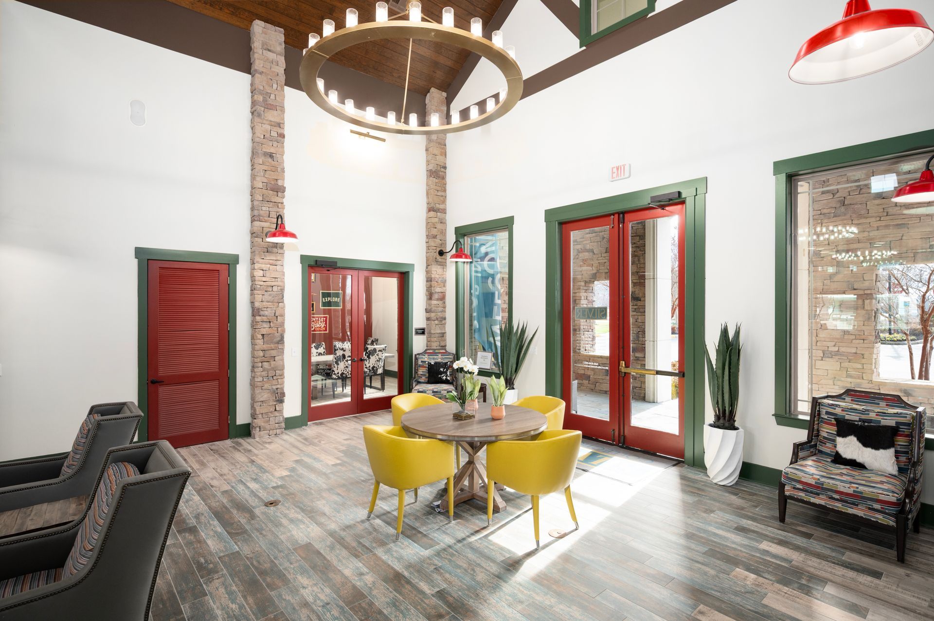 Modern lobby with wood floors, brick accents, yellow chairs around a table, and a large circular light fixture at Silver Collection at Cosner's Corner in Fredericksburg, VA.