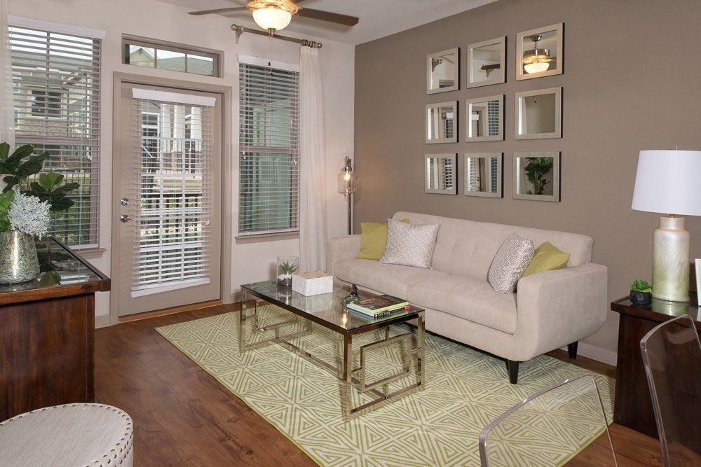 A beige sofa with pillows in a living room with a glass coffee table, patterned rug, and wall-mounted grid of mirrors.