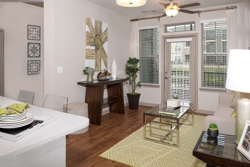 A living room with a console table, a glass coffee table on a yellow rug, and a glass door leading to an outdoor balcony at Silver Collection at Cosner's Corner in Fredericksburg, VA.