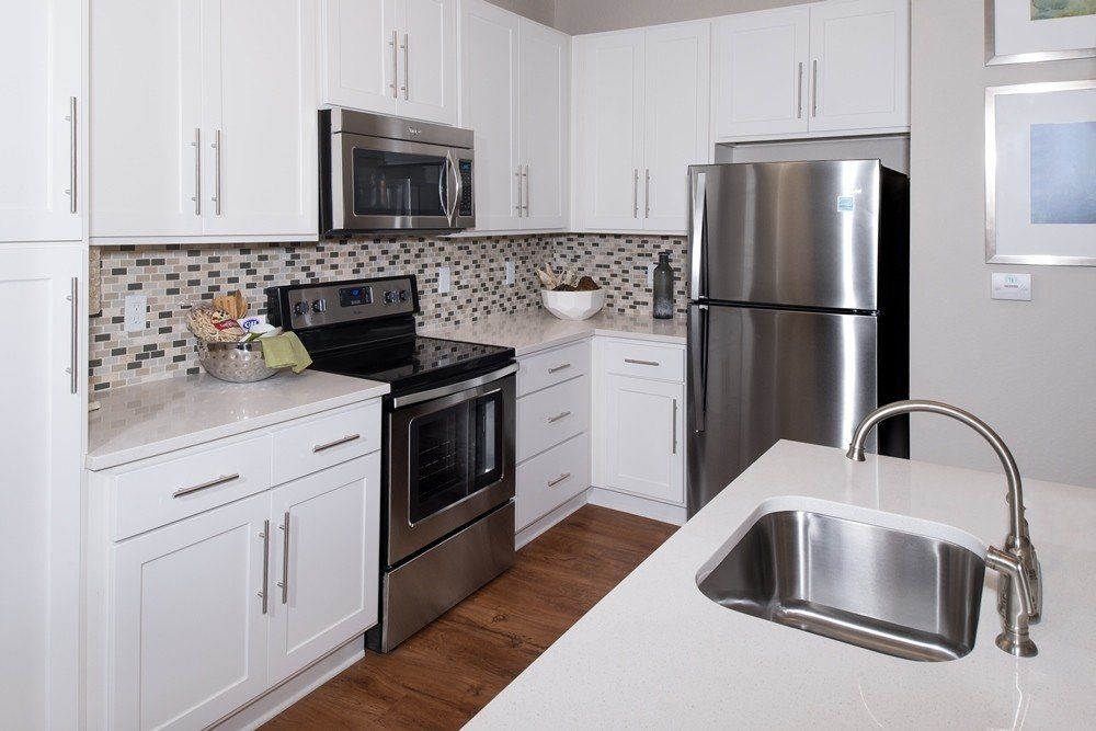 A modern kitchen featuring white cabinets, stainless steel appliances, a tiled backsplash, and an island with a sink.