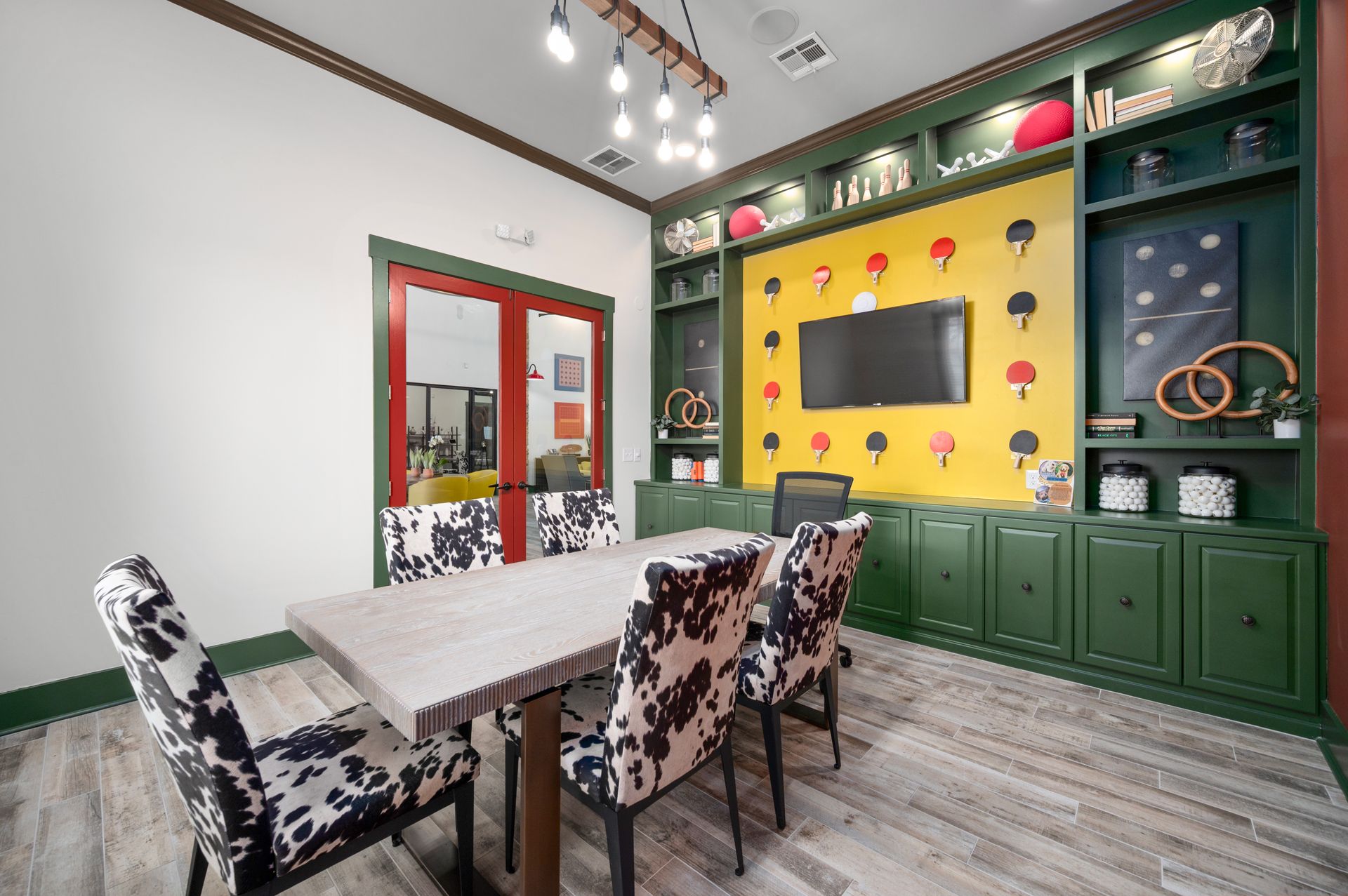 A modern meeting room with cow-print chairs, a long table, and a yellow wall display featuring ping pong paddle motifs.