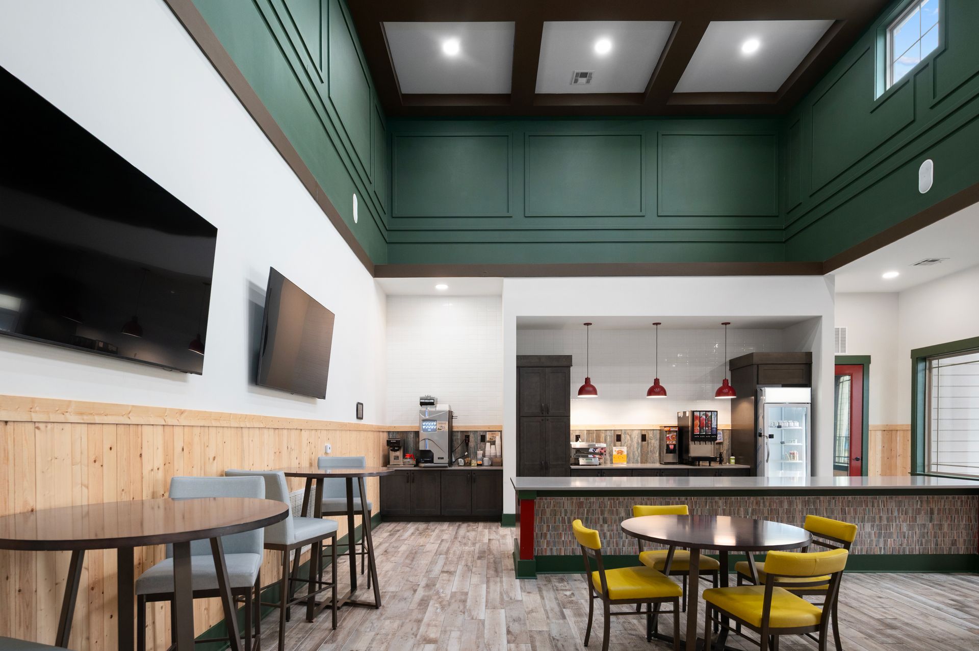Modern hotel breakfast area with high green-paneled ceilings, wooden wainscoting, seating tables, and a beverage station at Silver Collection at Cosner's Corner in Fredericksburg, VA.