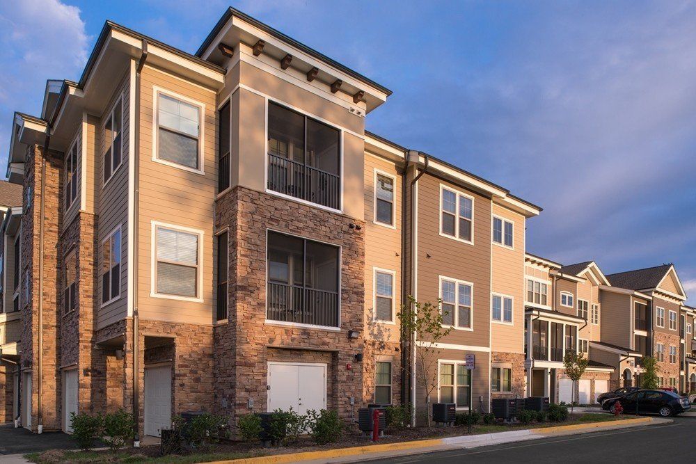 A multi-story apartment building with beige siding, brick accents, screened-in balconies, and a paved parking area at Silver Collection at Cosner's Corner in Fredericksburg, VA.