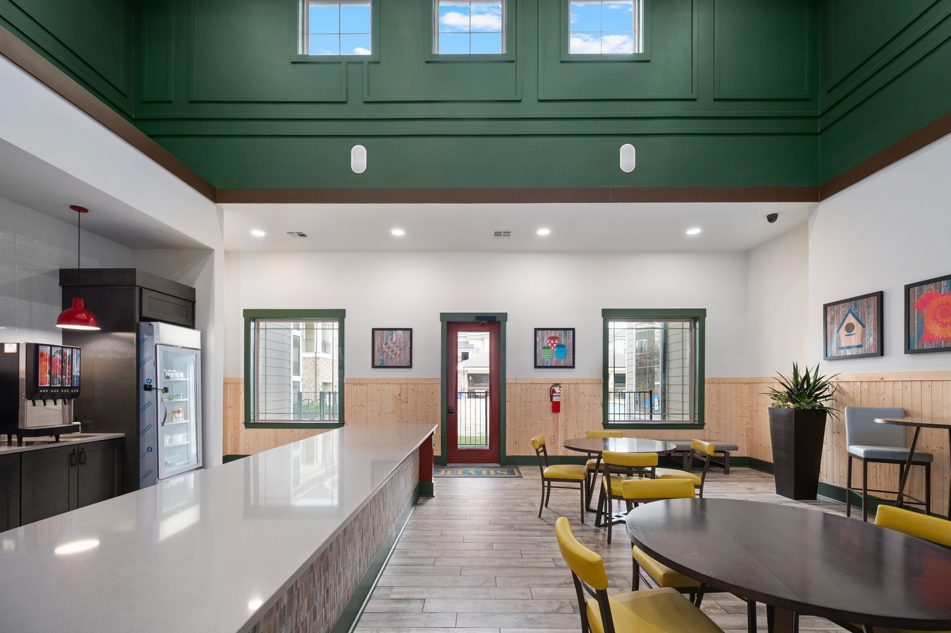 A bright, modern communal lobby with a white countertop, yellow chairs, wooden walls, and a green upper-level wall.