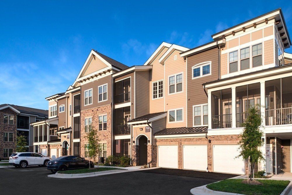 A multi-story apartment building with beige siding, brick accents, and attached garages under a clear blue sky at Silver Collection at Cosner's Corner in Fredericksburg, VA.