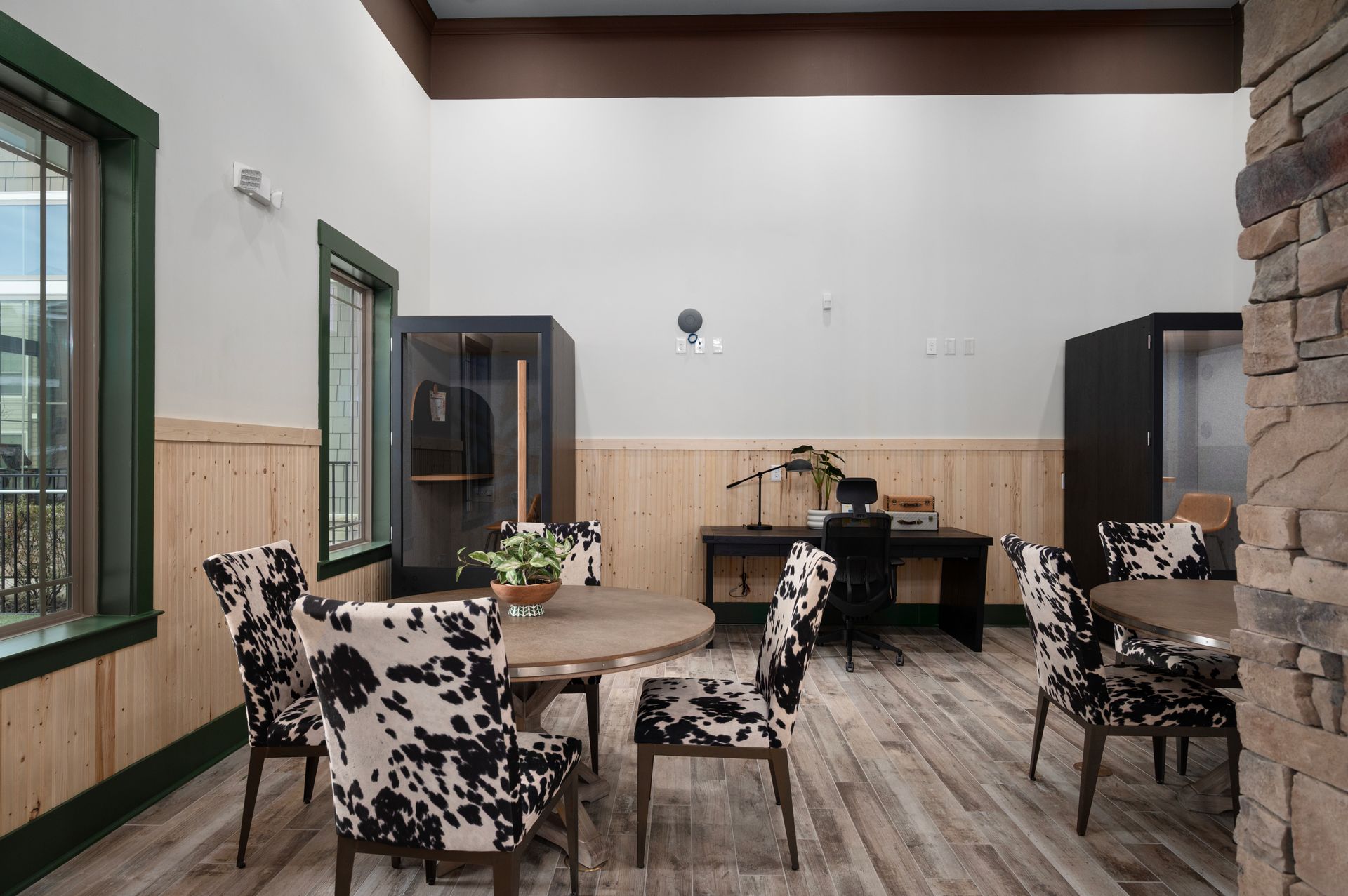 A rustic office space features a wooden table and desk with chairs upholstered in a black-and-white cow print pattern at Silver Collection at Cosner's Corner in Fredericksburg, VA.