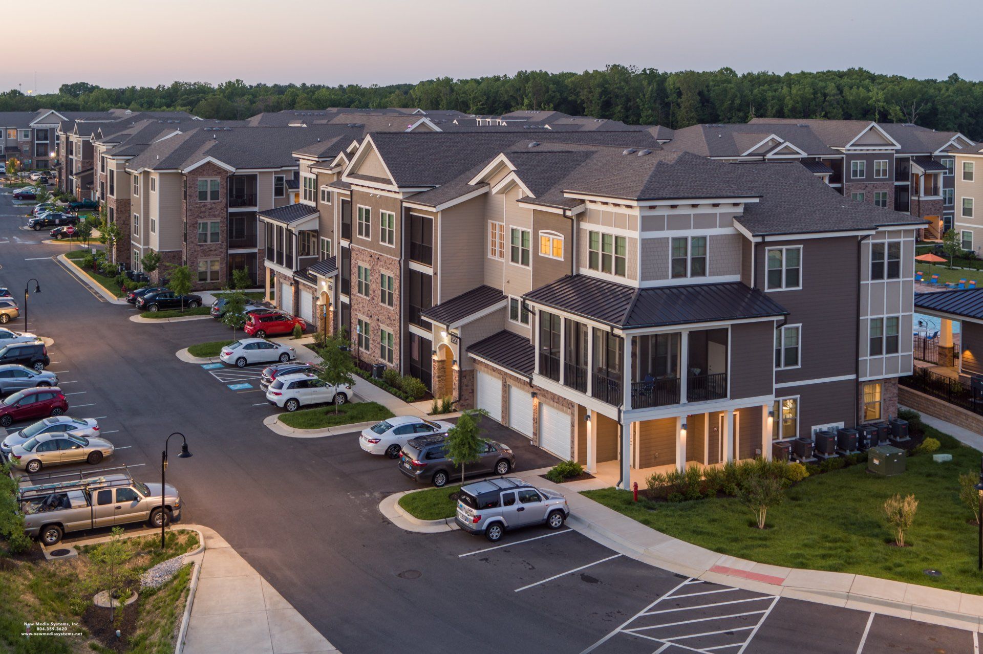 Aerial view of a multi-story apartment complex at dusk with parking lots containing several parked cars at Silver Collection at Cosner's Corner in Fredericksburg, VA.