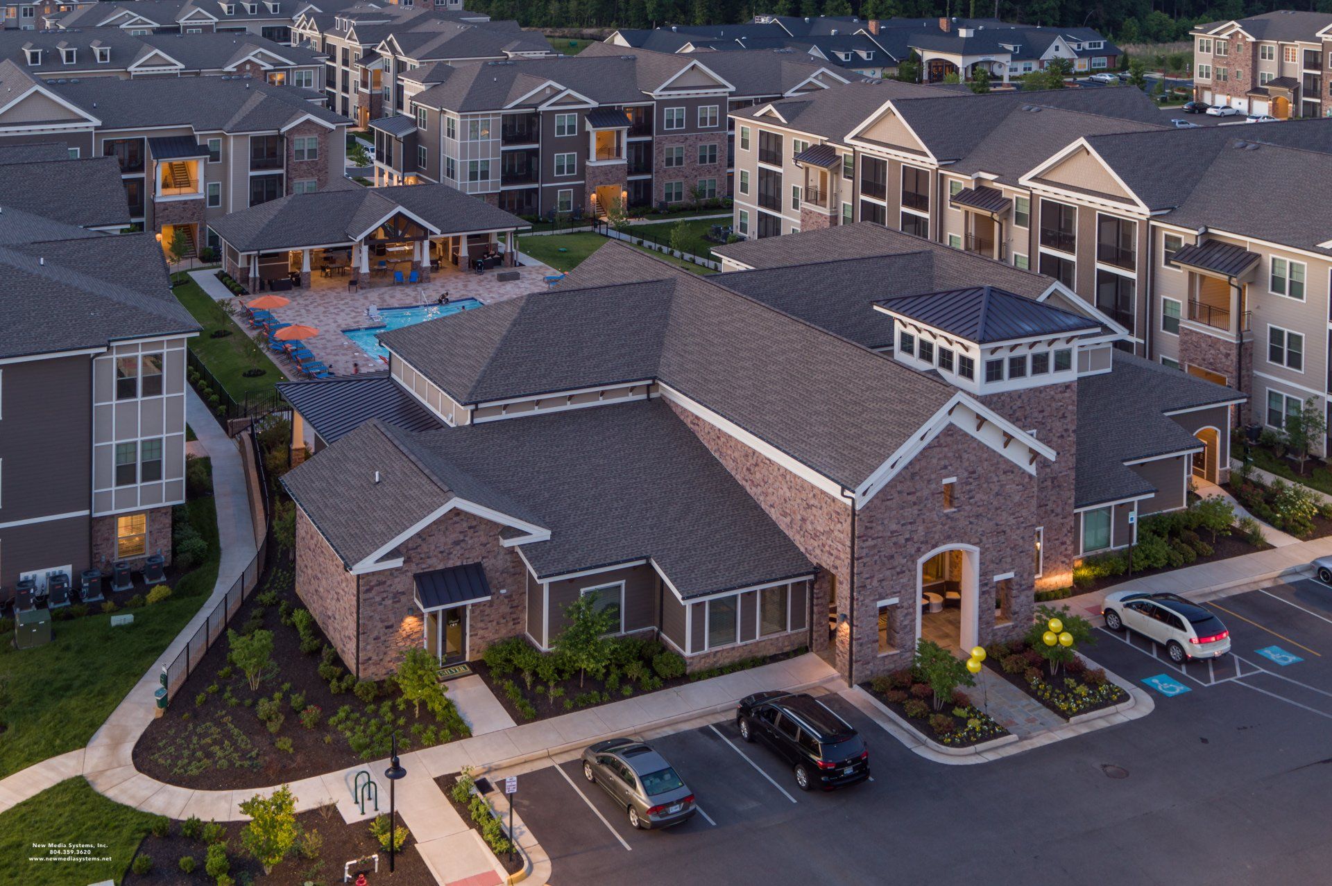 Aerial view of a multi-story apartment complex with brick buildings, a central clubhouse, and a swimming pool at Silver Collection at Cosner's Corner in Fredericksburg, VA.