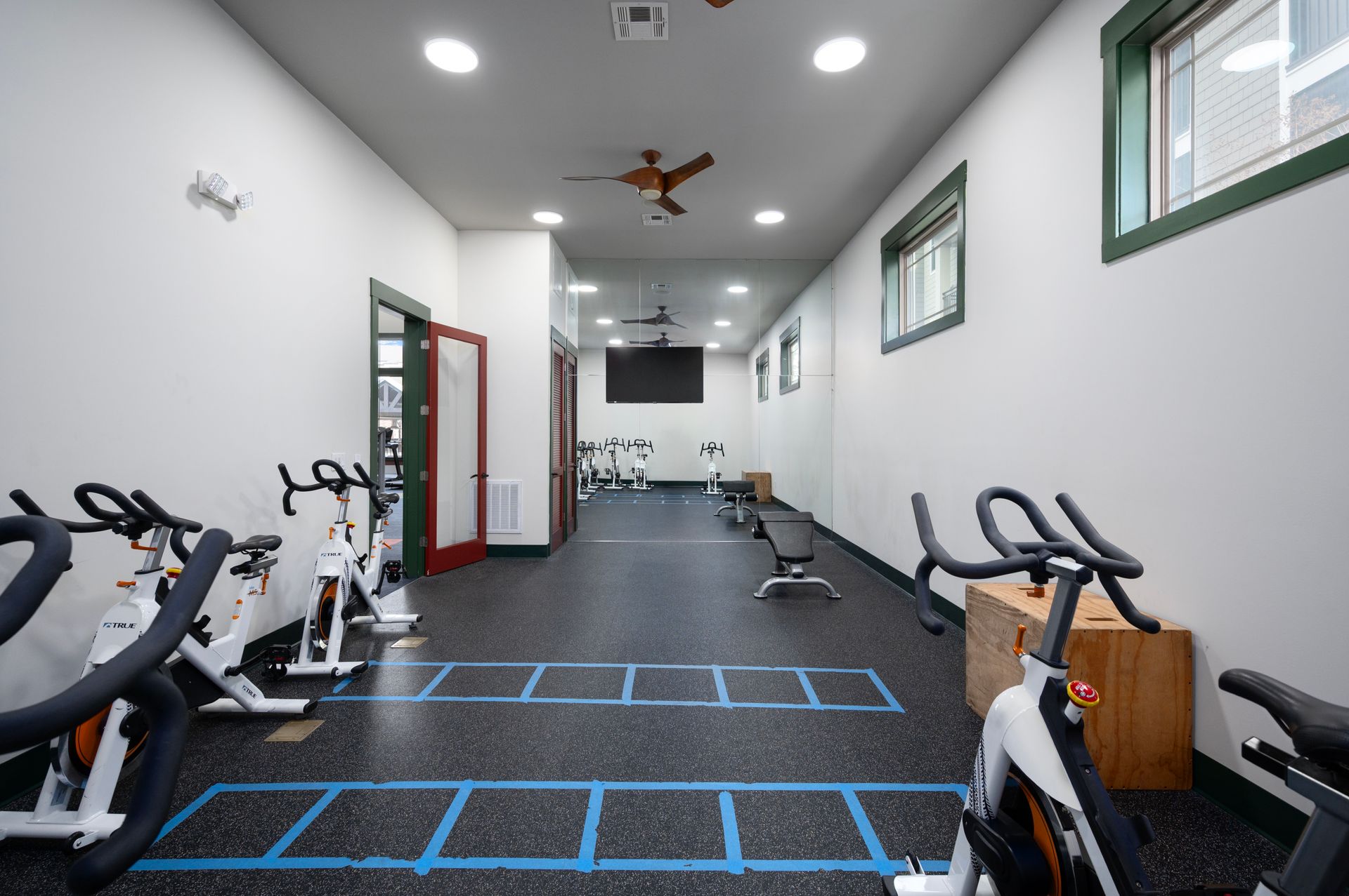 An indoor gym with stationary bikes, blue taped agility ladders on the floor, and a television mounted on the back wall at Silver Collection at Cosner's Corner in Fredericksburg, VA.