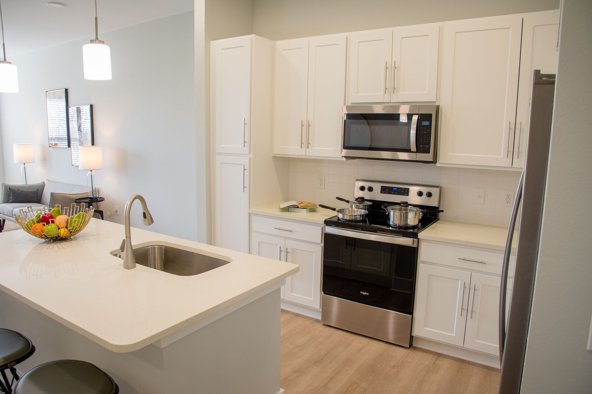 A modern kitchen with white cabinets, stainless steel appliances, a center island with a sink, and a fruit bowl.