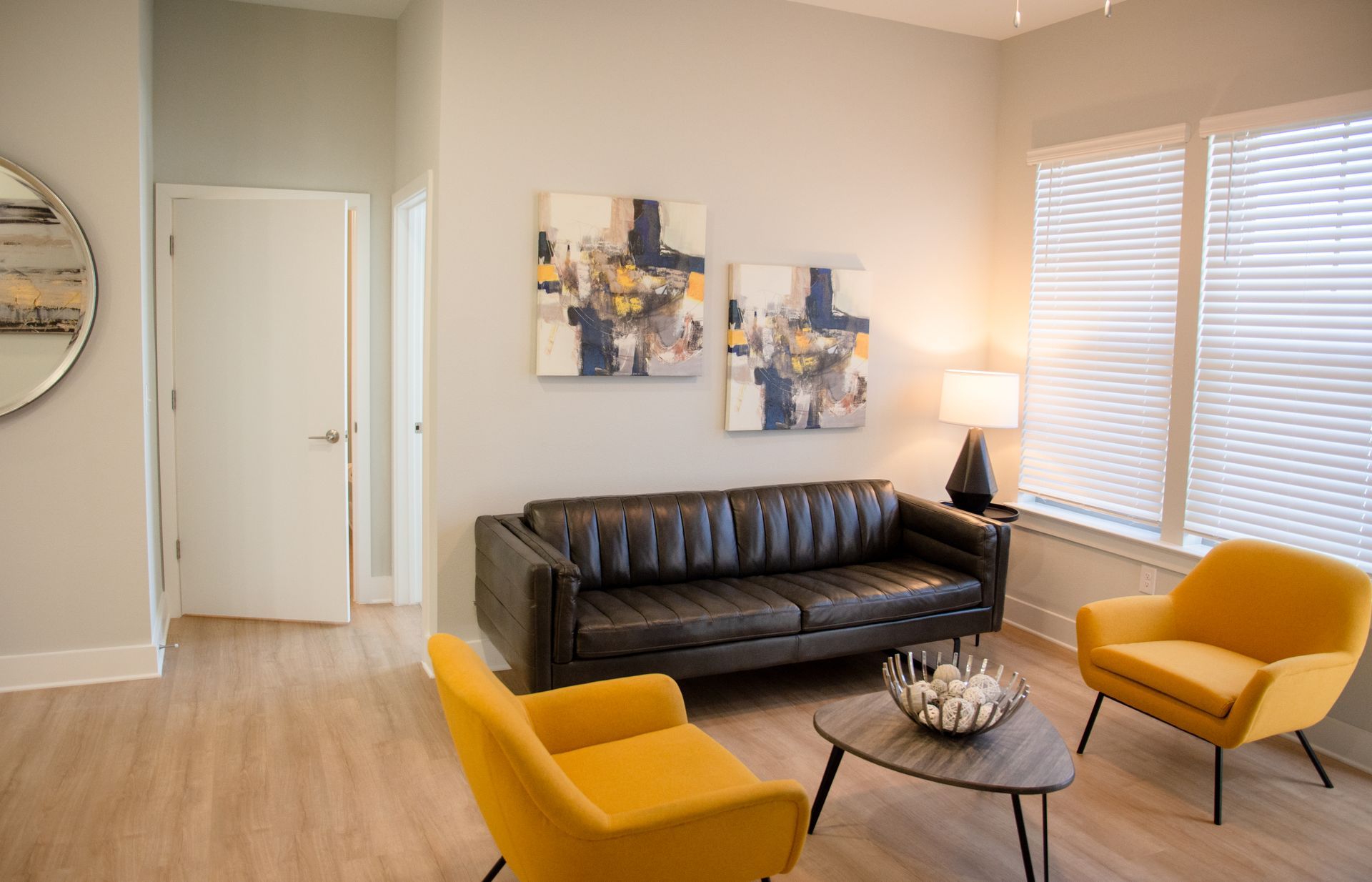 Living room with gray walls, wooden floors, leather sofa, two yellow chairs, and abstract art.