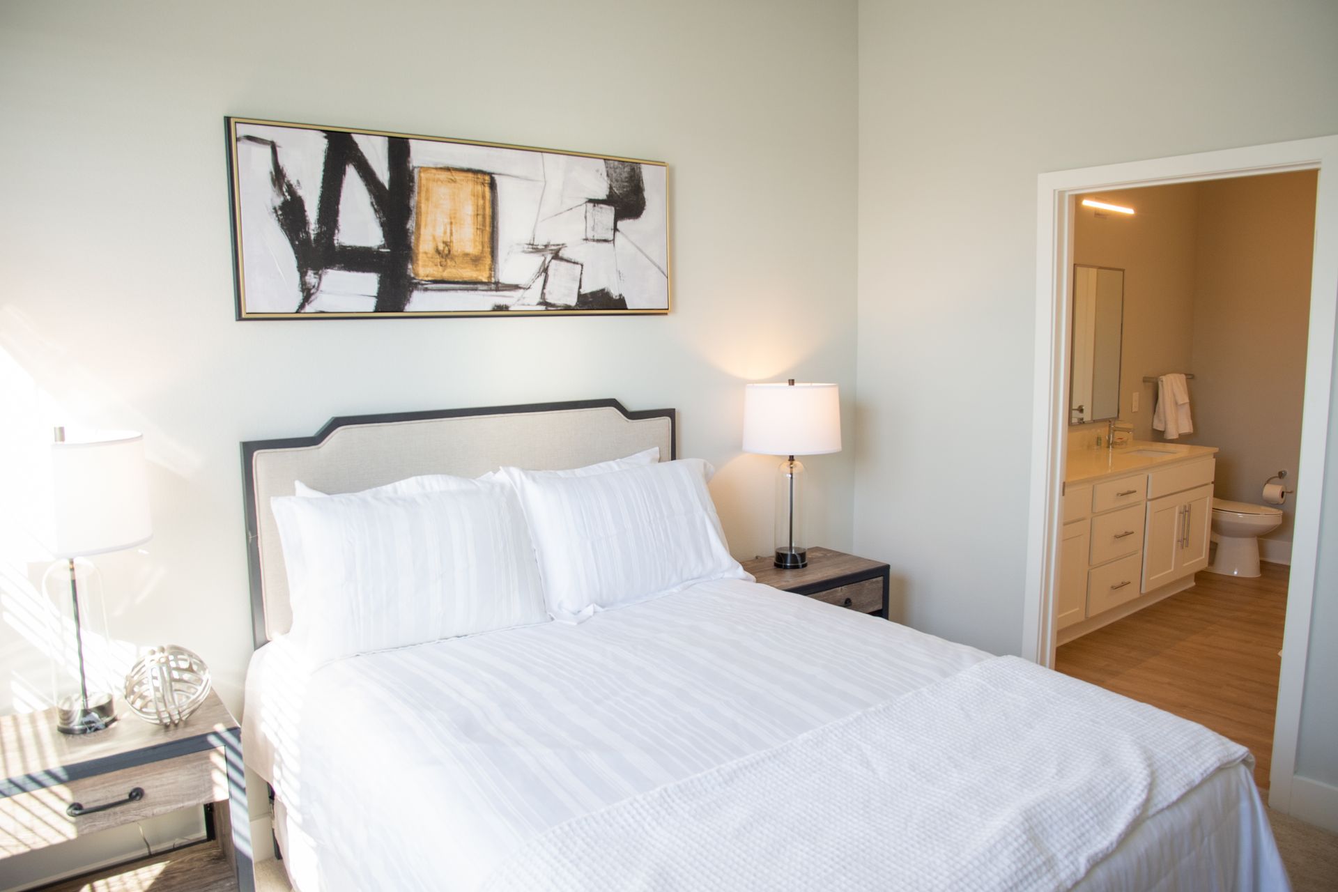 Bedroom with a bed, two nightstands, artwork, and an open doorway to a bathroom. The walls are light blue.