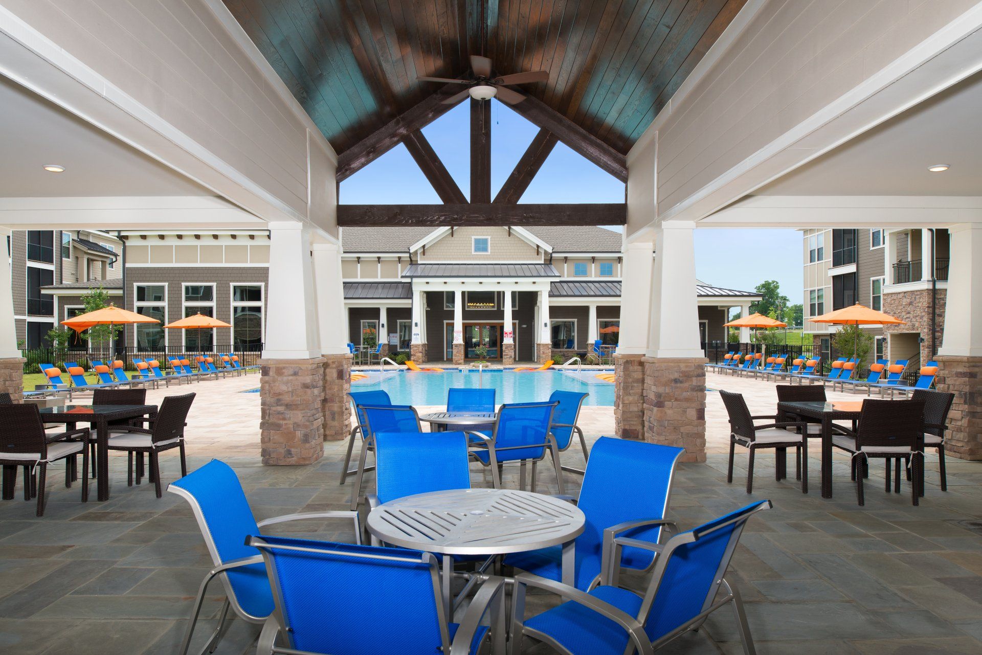 Outdoor patio with blue chairs and tables overlooking a swimming pool at a residential clubhouse at Silver Collection at Cosner's Corner in Fredericksburg, VA.