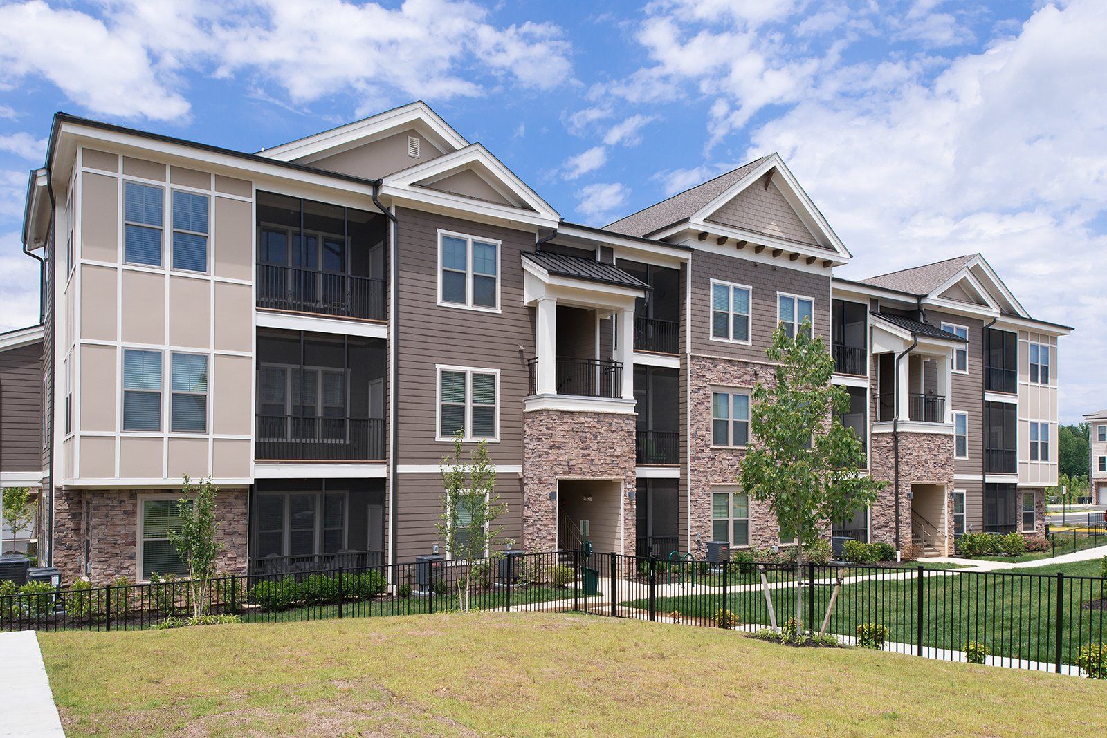 A three-story apartment building with beige siding, stone accents, and screened balconies under a cloudy blue sky at Silver Collection at Cosner's Corner in Fredericksburg, VA.