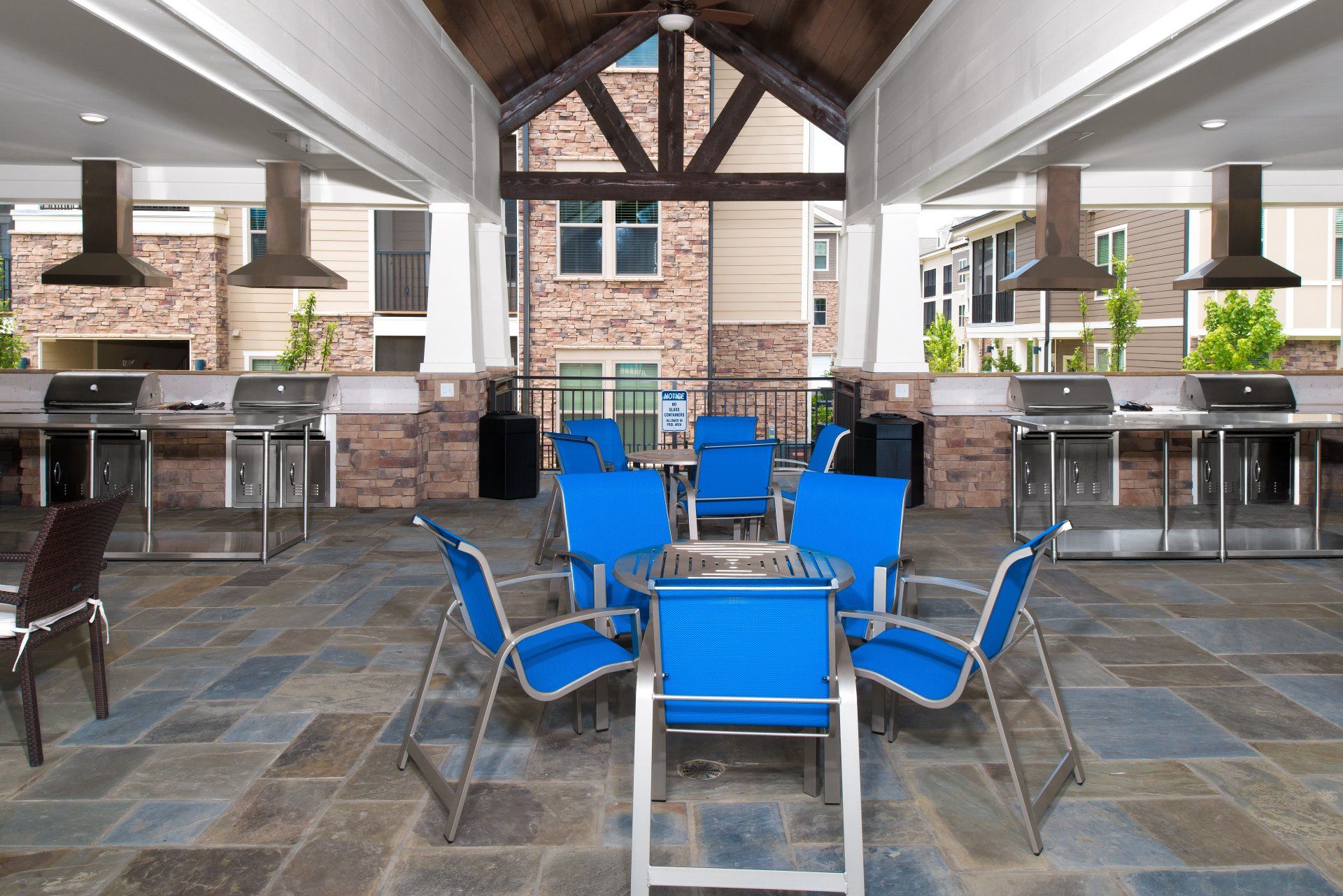 Outdoor patio with stone flooring, featuring several grills, dining tables, and blue chairs under a covered pavilion at Silver Collection at Cosner's Corner in Fredericksburg, VA.