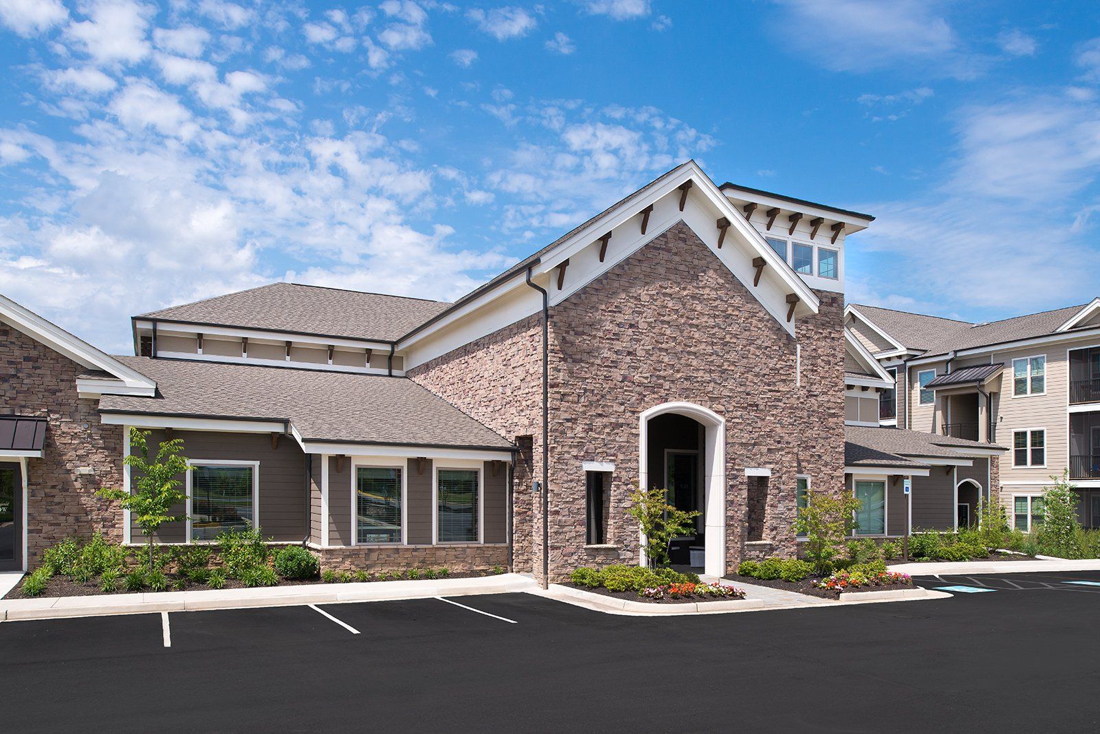 Stone-clad apartment complex leasing office with a gabled entrance, adjacent parking lot, and blue sky at Silver Collection at Cosner's Corner in Fredericksburg, VA.