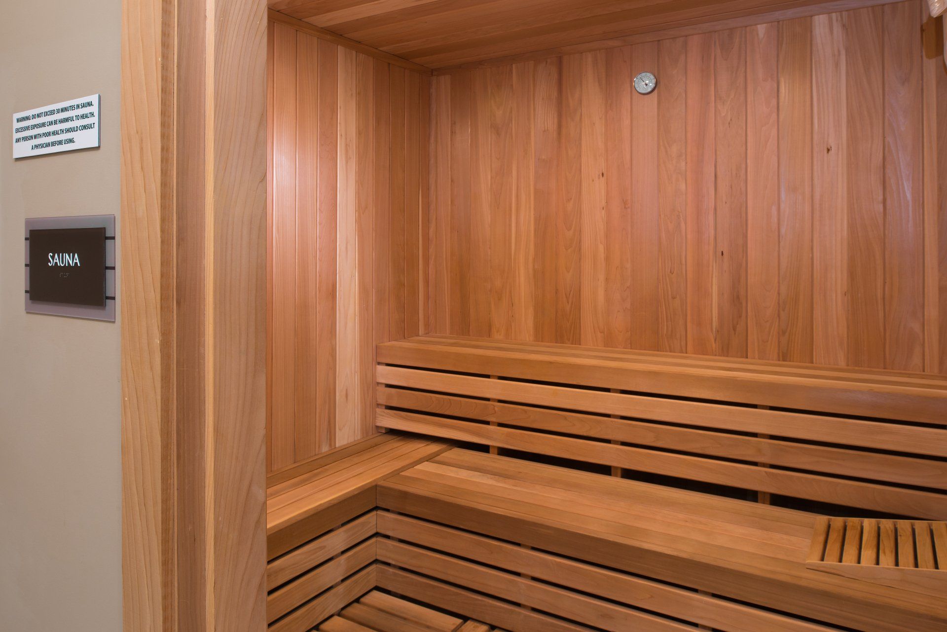 An empty cedar sauna room with slatted wood benches, viewed through a doorway marked with a sign at Silver Collection at Cosner's Corner in Fredericksburg, VA.