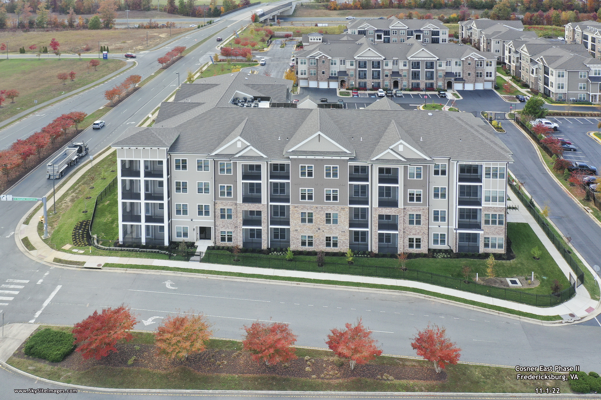 Aerial view of a multi-story apartment complex with light-colored facades, surrounded by roads and fall foliage.