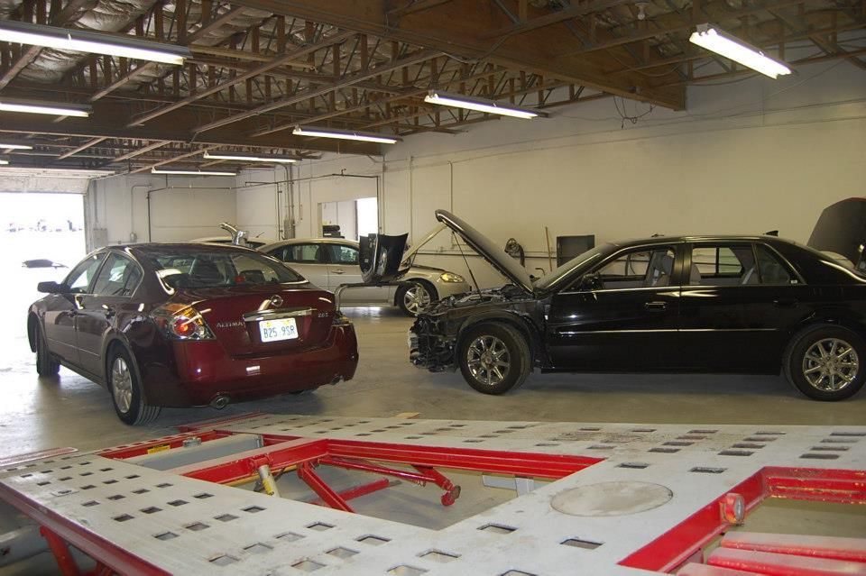 Two cars in a repair shop, with one raised on a red vehicle lift in the foreground.