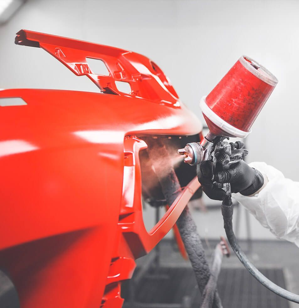 Worker spray-painting a glossy red car body panel in a workshop