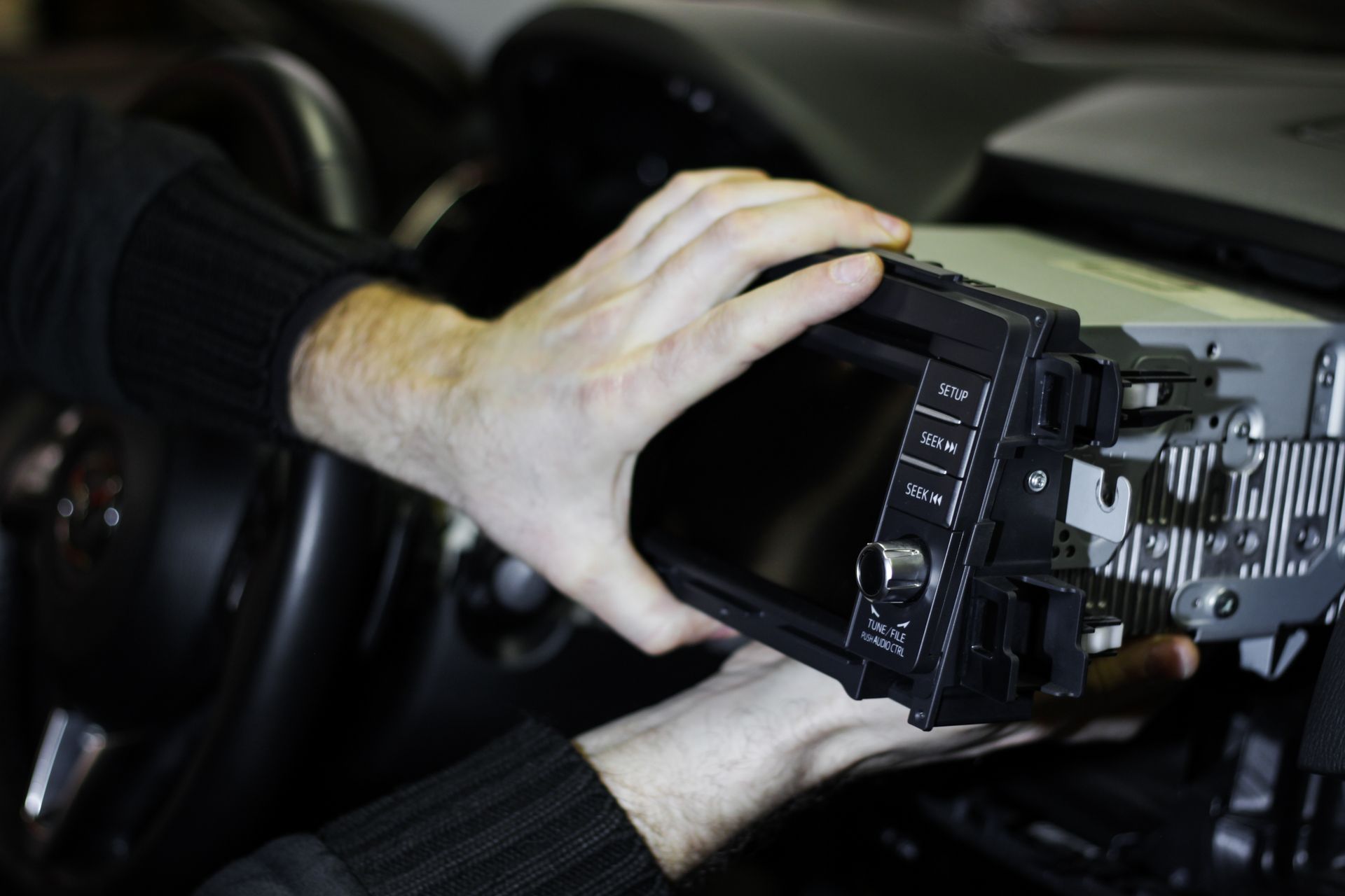 Hands adjusting a car stereo unit inside a vehicle dashboard