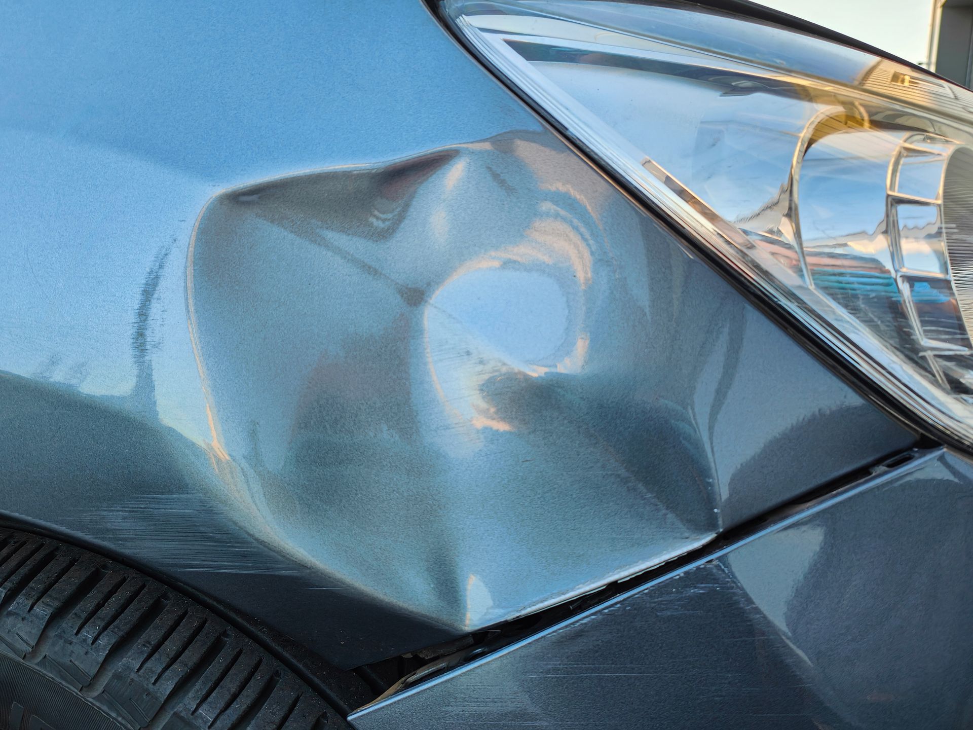 Damaged blue car front fender with a large dent near the headlight