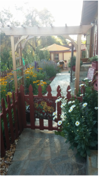 A wooden archway is surrounded by flowers and a fence in a garden.