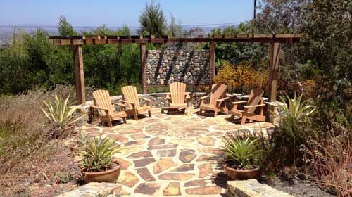 A stone patio with chairs and a pergola in the background
