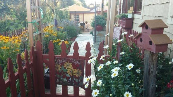 A red picket fence is surrounded by flowers and a birdhouse.