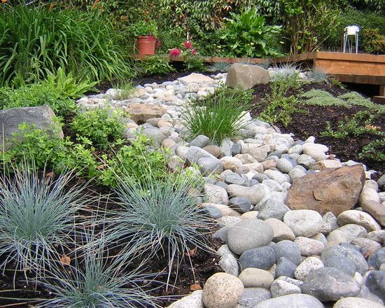 A garden filled with rocks and plants with a wooden bridge in the background.