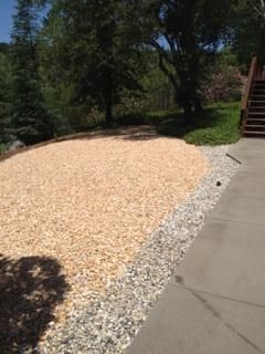 A pile of wood chips is sitting next to a concrete driveway.