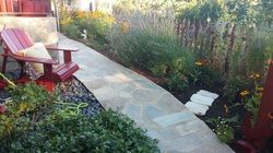 A wooden chair is sitting on a stone walkway in a garden.