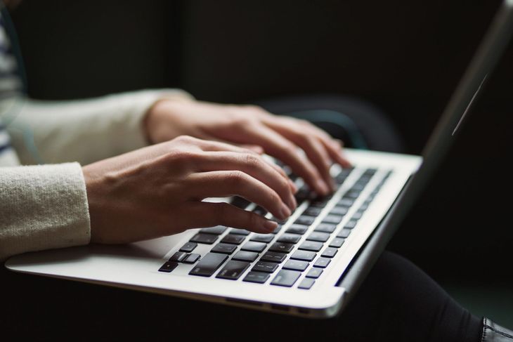 Hands typing on a silver laptop keyboard in a dimly lit setting