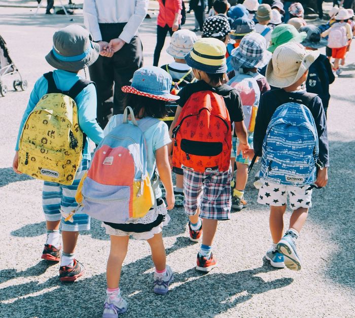 Children wearing colorful backpacks walking together outdoors on a sunny day