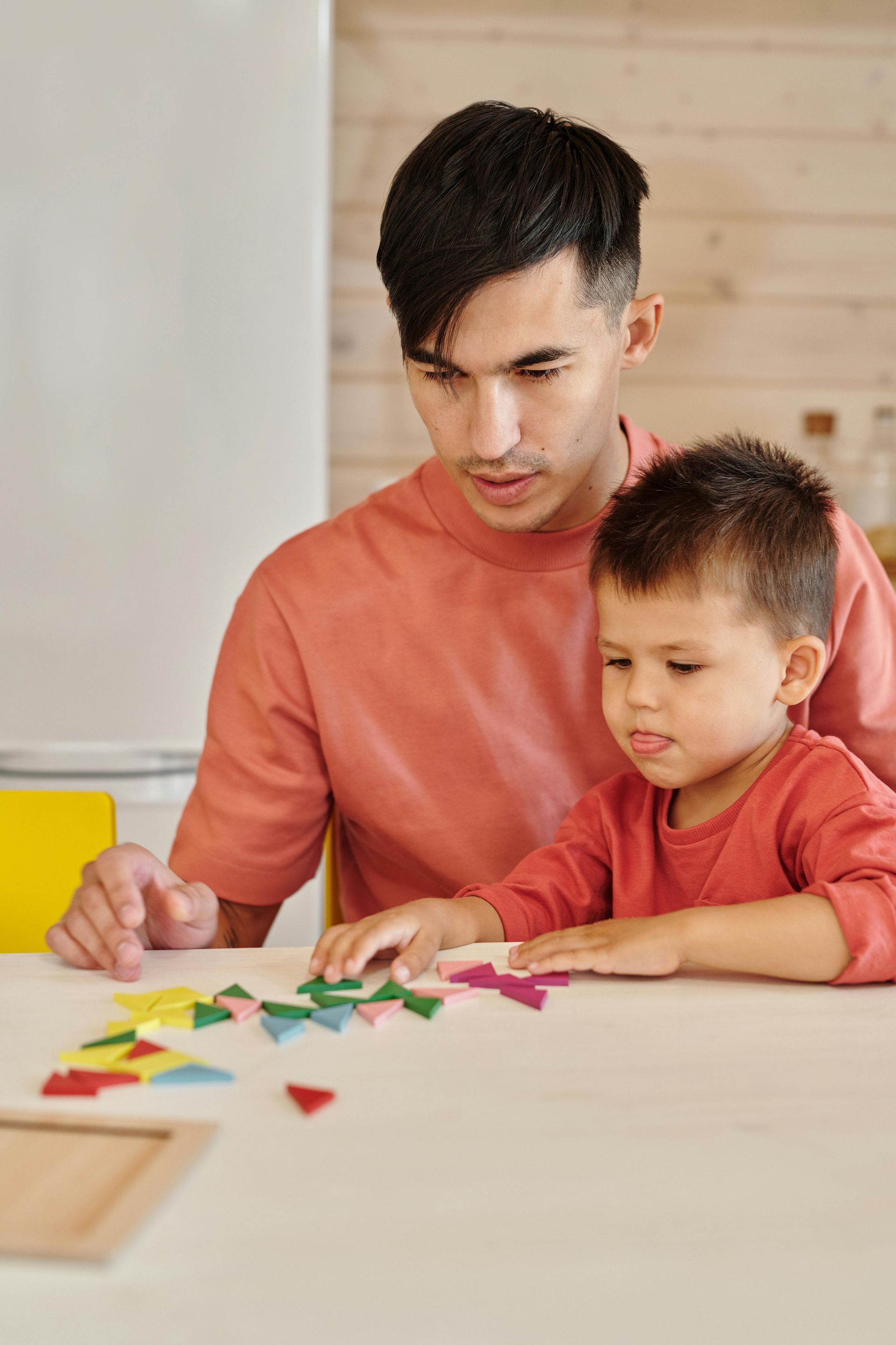 Adult and child seated at a table, arranging colorful geometric pieces in a craft activity.