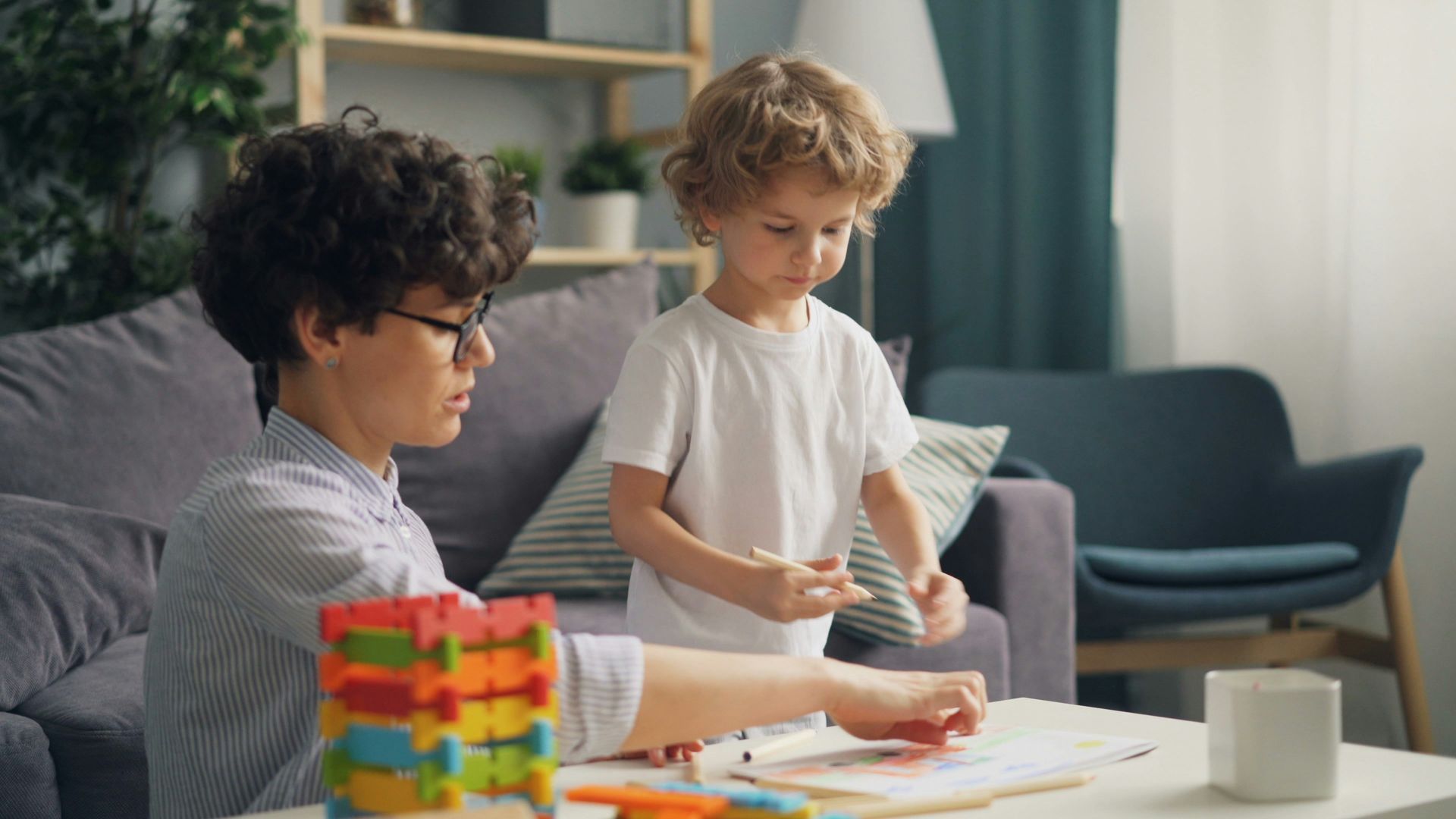 Two children playing with colorful blocks and drawing at a table in a cozy living room