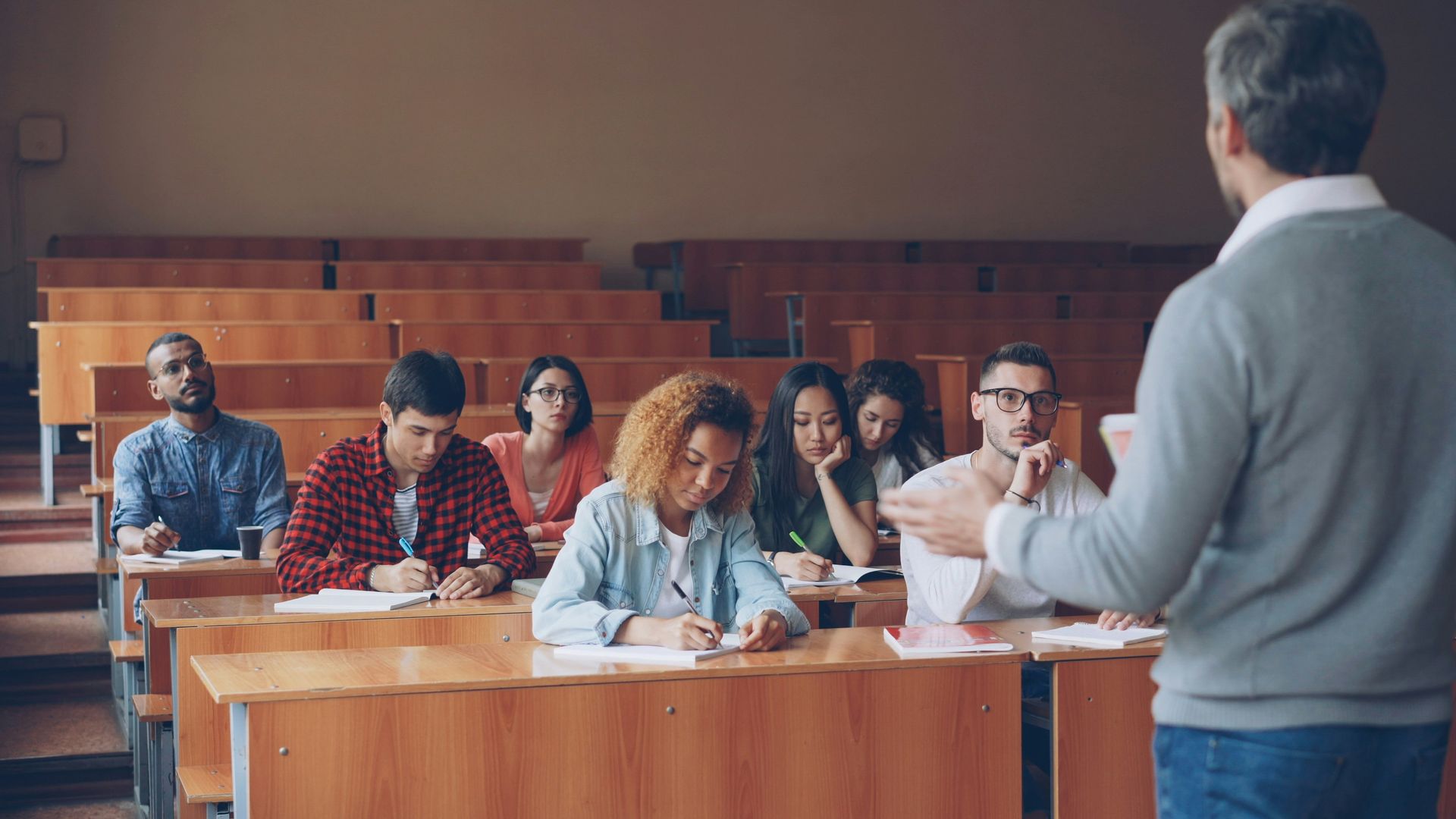 Classroom lecture with students seated at desks, listening to a teacher at the front